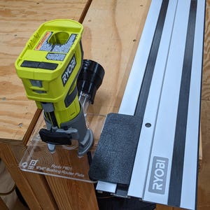 Puede incluir: Una fresadora Ryobi amarilla y gris con un accesorio negro y un riel guía plateado y negro. La fresadora está sobre una base de plástico transparente. El texto "Ryobi P601 6 1/8" Bushing Router Plate" es visible.