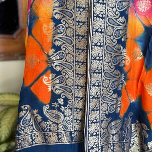 May include: A blue and orange tie-dye fabric scarf with a gold paisley border.