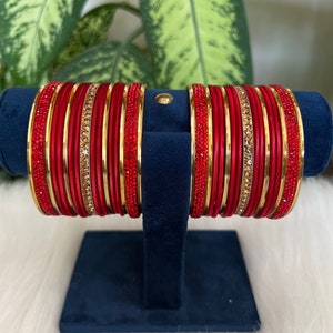 May include: A set of red and gold bangles with rhinestones. The bangles are stacked on a blue velvet stand.