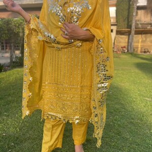 May include: A yellow salwar kameez with silver embroidery and mirror work. The outfit includes a long-sleeved top, pants, and a dupatta.