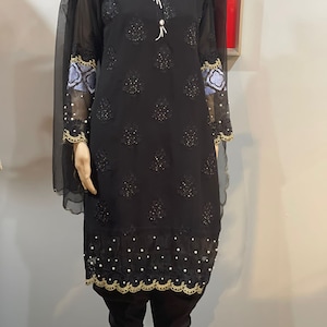 May include: A black long-sleeved dress with intricate embroidery and pearl accents. The dress has a round neckline and a flowing silhouette. It is paired with black pants and a sheer black dupatta.