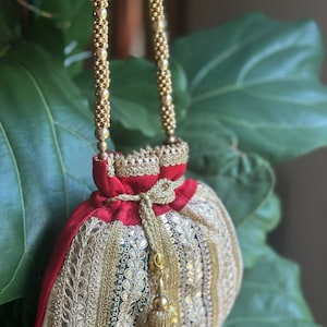 May include: A red and gold embroidered drawstring bag with a gold beaded chain strap and a tassel.