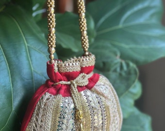 May include: A red and gold embroidered drawstring bag with a gold beaded chain strap and a tassel.