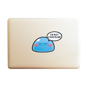 May include: A light beige laptop with a blue and pink cartoon slime character sticker. The sticker has a speech bubble that says "I'm not a bad slime".