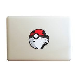May include: A white laptop with a red, white, and black Pokeball sticker on the lid. The Pokeball is cracked and has a black outline.