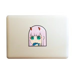 May include: A pink-haired anime character with red horns and green eyes is eating a blue fish. The character is looking at the viewer with a surprised expression. The image is a sticker on a laptop.
