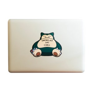 May include: A white laptop with a green Snorlax sticker. The sticker shows Snorlax sitting with a remote control and the text "Snorlax and Chill".