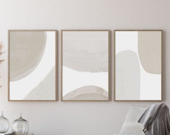Peut inclure: Trois impressions d'art abstrait avec des coups de pinceau et des formes beige et blanc. Les impressions sont encadrées dans du bois naturel et accrochées à un mur blanc.