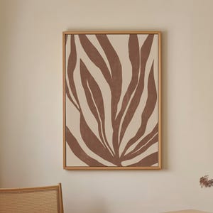 May include: A framed abstract art print with a brown and white leaf design. The print is hanging on a light beige wall.
