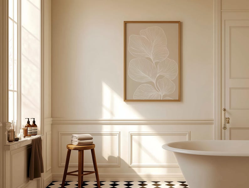 Puede incluir: Un ba&ntilde;o blanco con una ba&ntilde;era independiente, un taburete de madera con toallas y una impresi&oacute;n enmarcada de un dibujo de l&iacute;nea blanca de una planta sobre un fondo beige.