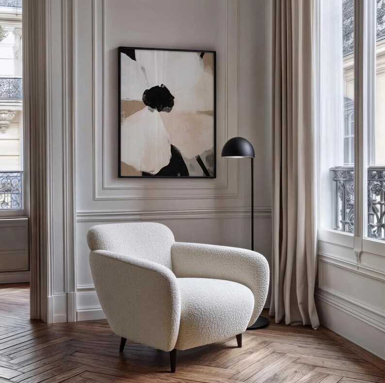 May include: A modern living room scene featuring a cream-colored, rounded armchair with dark legs. A black floor lamp stands beside the chair. A large abstract floral painting in a black frame hangs on the wall. The room has a neutral color palette.