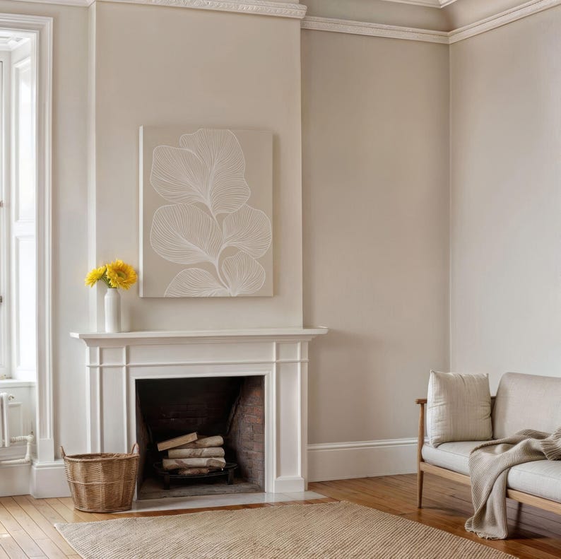 Puede incluir: Una repisa de chimenea blanca con una impresi&oacute;n de lienzo enmarcada en blanco de un dise&ntilde;o floral estilizado encima. La chimenea tiene un hogar de ladrillo y un hogar de le&ntilde;a. Una cesta de mimbre se encuentra en el suelo frente a la chimenea.