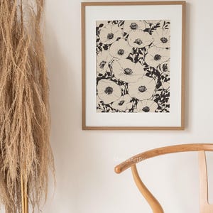 K&ouml;nnte beinhalten: Ein Schwarz-Wei&szlig;-Linienkunst-Druck eines floralen Designs mit einer Ansammlung von Mohnblumen. Der Druck ist in einem hellbraunen Holzrahmen gerahmt und h&auml;ngt an einer wei&szlig;en Wand.