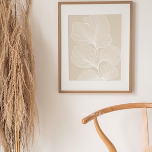 Puede incluir: Una impresi&oacute;n enmarcada con un fondo beige y un dibujo de l&iacute;nea blanca de una planta estilizada con hojas. El marco es de color madera claro.