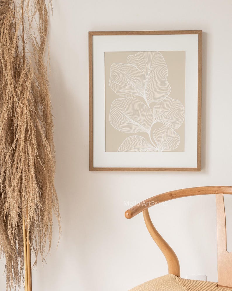 Puede incluir: Una impresi&oacute;n enmarcada con un fondo beige y un dibujo de l&iacute;nea blanca de una planta estilizada con hojas. El marco es de color madera claro.