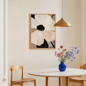 May include: A framed abstract floral art print with beige, black, and white colors hangs above a round white table. A blue vase holds a bouquet of flowers. Two wooden chairs are positioned near the table, and a gold pendant light hangs from the ceiling.