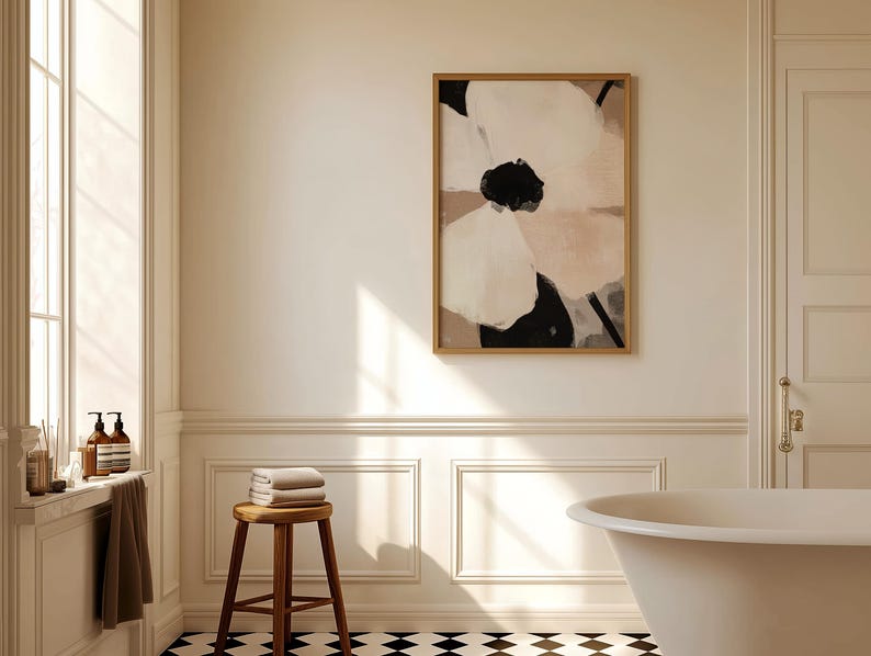 May include: A white bathtub with a black and white checkered floor. A wooden stool with towels on top is in the foreground. A framed abstract painting of a white and pink flower is on the wall. The bathroom has white walls and trim.