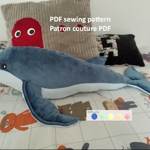 May include: A blue whale plush toy with a white belly. The whale is lying on a white and grey patterned fabric with the text "PDF sewing pattern Patron couture PDF" and a difficulty rating scale.