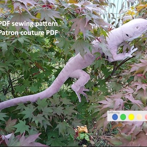Peut inclure: Une iguane en peluche violet clair perchée dans un arbre feuillu. L'iguane a une longue queue et des détails précis. Le texte sur l'image indique "PDF sewing pattern Patron couture PDF". Un indicateur de niveau de difficulté est également présent.