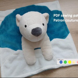 Peut inclure: Un ours polaire en peluche avec un nez gris et des yeux noirs est posé sur une couverture blanche et bleue. La couverture présente un motif de montagne bleu. Le texte sur l'image indique "PDF sewing pattern Patron couture PDF".