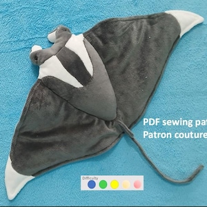 Puede incluir: Un peluche gris en forma de manta raya con detalles blancos y una larga cola, sobre un fondo azul. El texto "PDF sewing pattern Patron couture PDF" es visible. También hay un indicador de nivel de dificultad.