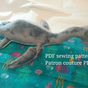 May include: A gray plush sea monster toy on a blue fabric with a sea-themed pattern. The text "PDF sewing pattern Patron couture PDF" is visible on the fabric.