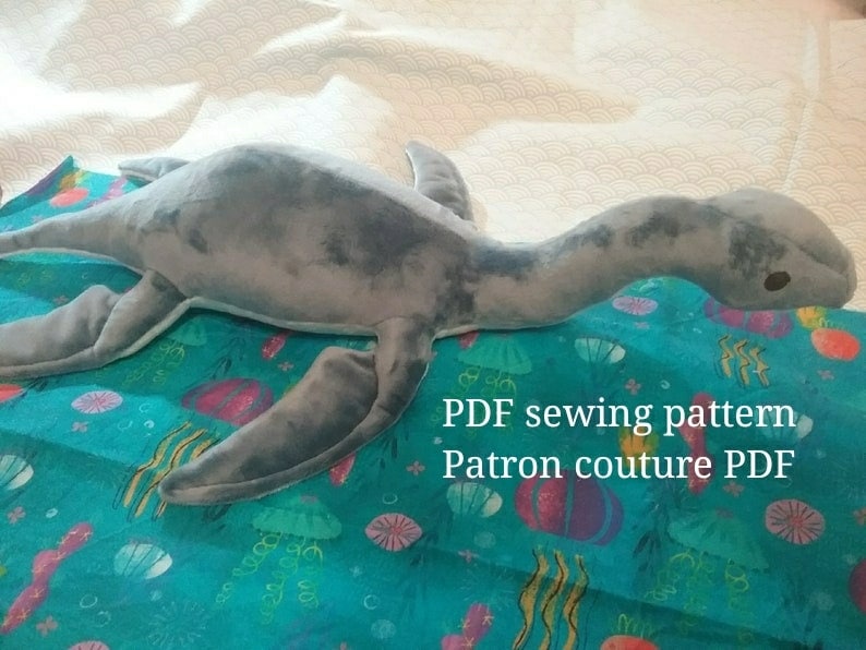 May include: A gray plush sea monster toy on a blue fabric with a sea-themed pattern. The text "PDF sewing pattern Patron couture PDF" is visible on the fabric.
