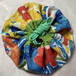 May include: A colorful drawstring bag with a green drawstring and a floral pattern in shades of blue, yellow, red, and orange.