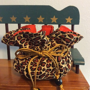 May include: A small leopard print drawstring bag with a gold cord and black beads. The bag is sitting on a wooden chair with a green back.