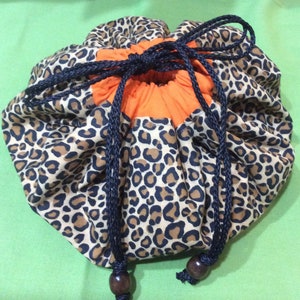 May include: A leopard print drawstring bag with a bright orange lining. The bag is made of fabric and has a black drawstring closure.