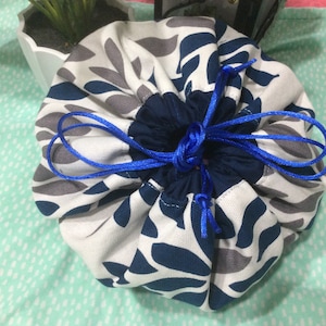 May include: A white drawstring bag with a blue and gray floral pattern. The bag is cinched closed with a blue cord.