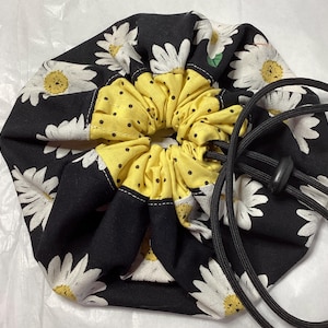 May include: A black drawstring bag with a white daisy print. The bag has a yellow polka dot lining and a black drawstring.
