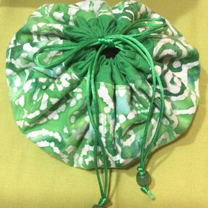 May include: A green and white drawstring bag with a batik pattern. The bag has a green satin ribbon and green jade beads on the drawstrings.