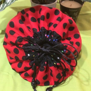 May include: Red drawstring bag with black polka dots and a black drawstring with black beads. The bag is gathered at the top and has a black lining with colorful polka dots.