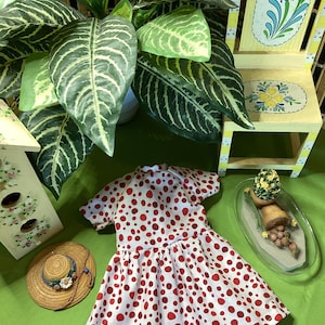 May include: A white dress with red polka dots, a straw hat, and a small potted plant on a tray. The dress has short sleeves and a gathered skirt.