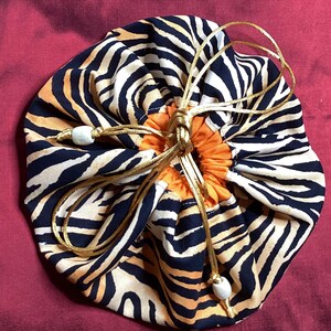 May include: A drawstring bag with a tiger print design. The bag is made of fabric and has a gold drawstring. The bag is closed and has a white bead on the drawstring.