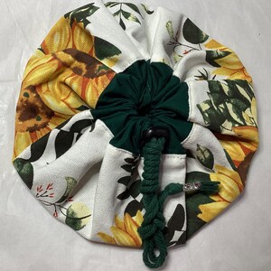 May include: A white drawstring bag with a green drawstring and a sunflower print. The bag is made of canvas and has a round shape.