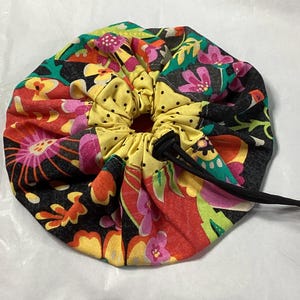 May include: A colorful drawstring bag with a floral pattern in shades of red, yellow, pink, green, and black. The bag is made of fabric and has a drawstring closure.