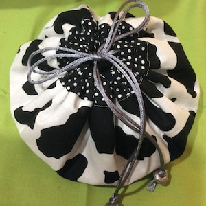 May include: A black and white cow print drawstring bag with a silver cord and silver beads. The bag is gathered at the top and has a polka dot lining.