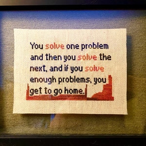 May include: A framed cross-stitch with the text "You solve one problem and then you solve the next, and if you solve enough problems, you get to go home."