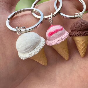 K&ouml;nnte beinhalten: Vier Schl&uuml;sselanh&auml;nger in Form von Eiswaffeln mit verschiedenen Geschmacksrichtungen: wei&szlig;, rosa und wei&szlig;er Swirl, braun und gr&uuml;n. Jeder Schl&uuml;sselanh&auml;nger ist an einem silbernen Schl&uuml;sselring befestigt.