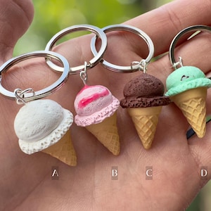 K&ouml;nnte beinhalten: Vier Schl&uuml;sselanh&auml;nger in Form von Eiswaffeln mit verschiedenen Geschmacksrichtungen: wei&szlig;, rosa und wei&szlig;er Swirl, Schokolade und gr&uuml;n. Jeder Schl&uuml;sselanh&auml;nger ist an einem silbernen Schl&uuml;sselring befestigt.