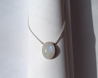 May include: A silver necklace featuring an oval moonstone pendant. The moonstone has a pearly white color with blue and iridescent flashes. The pendant is set in a silver bezel and hangs from a delicate silver chain. The jewelry is displayed on a white background.