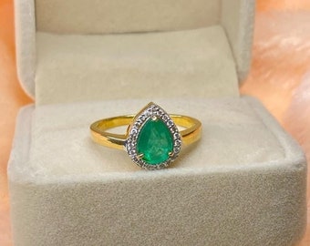 May include: A pear-shaped emerald gemstone ring set in a gold band with a halo of smaller diamonds.