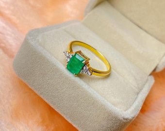 May include: A gold ring with a large emerald green gemstone surrounded by smaller clear gemstones. The ring is in a white velvet ring box.