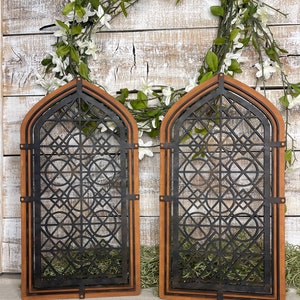 May include: Two wooden framed black metal lattice panels with a geometric design. The panels are set against a white wood background.