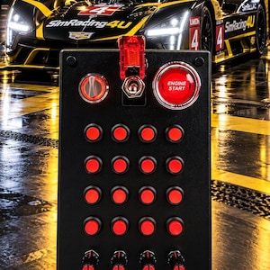 May include: A black rectangular button box controller featuring a grid of sixteen red push buttons, four red rotary knobs, a red safety toggle switch, and a large red illuminated push button labelled ENGINE START in white text.