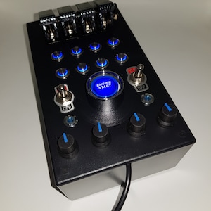 May include: A black box with a blue illuminated button that says "Engine Start" and several other blue illuminated buttons. There are also four black knobs with blue accents and two toggle switches labelled "OFF".