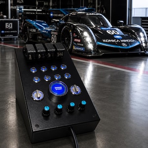May include: A black angled control panel featuring a large central blue illuminated Engine Start button, multiple smaller blue LED push buttons, two silver rotary switches, and four black knobs with blue indicators, connected by a black cable.