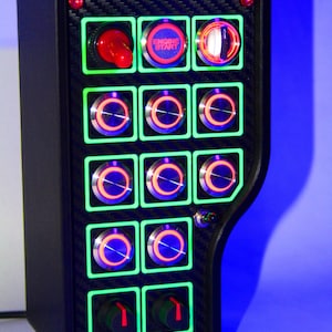 May include: A black panel with a carbon fiber texture and multiple illuminated buttons. The buttons are arranged in a grid pattern and have green, red, and blue lights. One button reads "Engine Start".